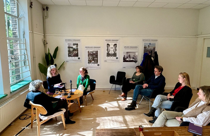Foto van de podcastopname met Anita Blom. De interviewer en de geïnterviewden zitten bij het raam, de bezoekers kijken toe.